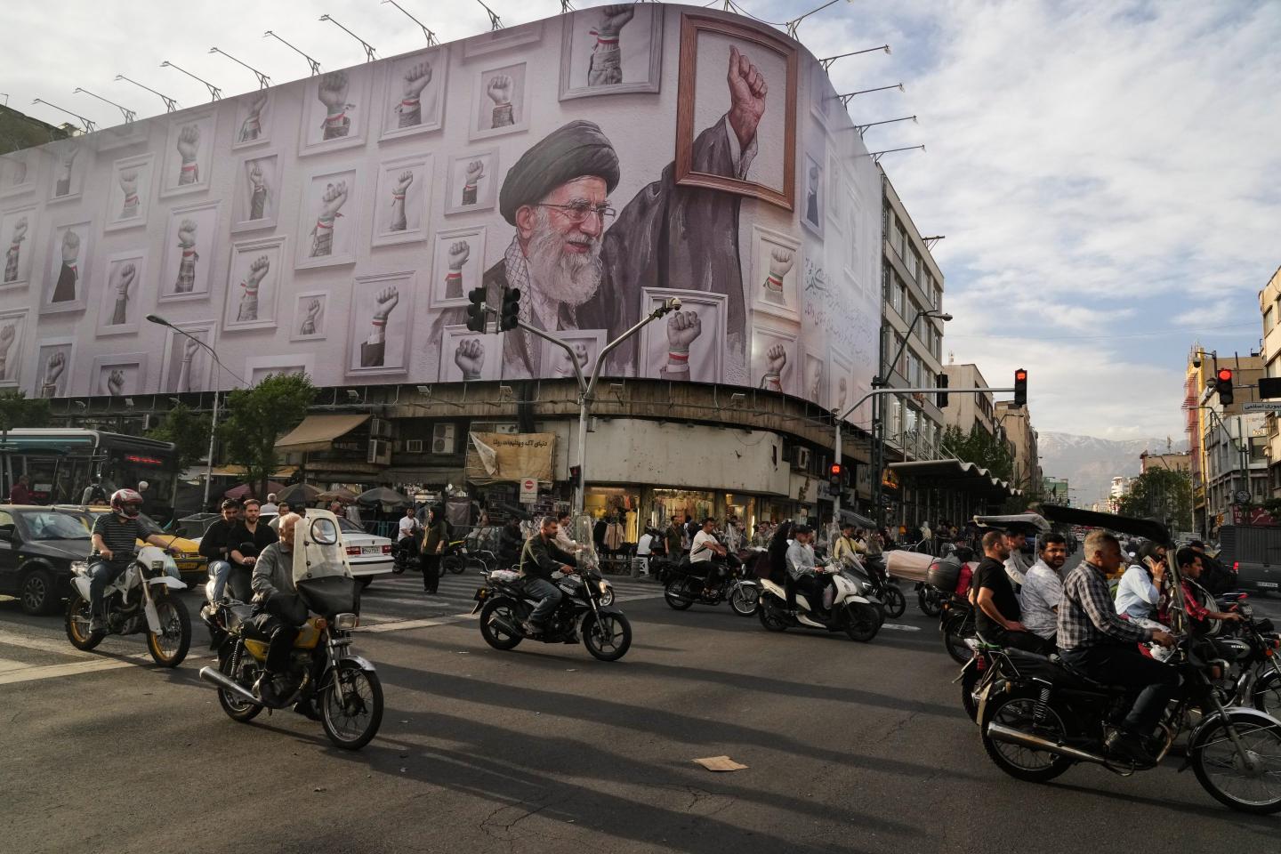 Motorbikes drive past a billboard with graphic showing the late Iranian Supreme Leader Ayatollah Ali Khamenei
