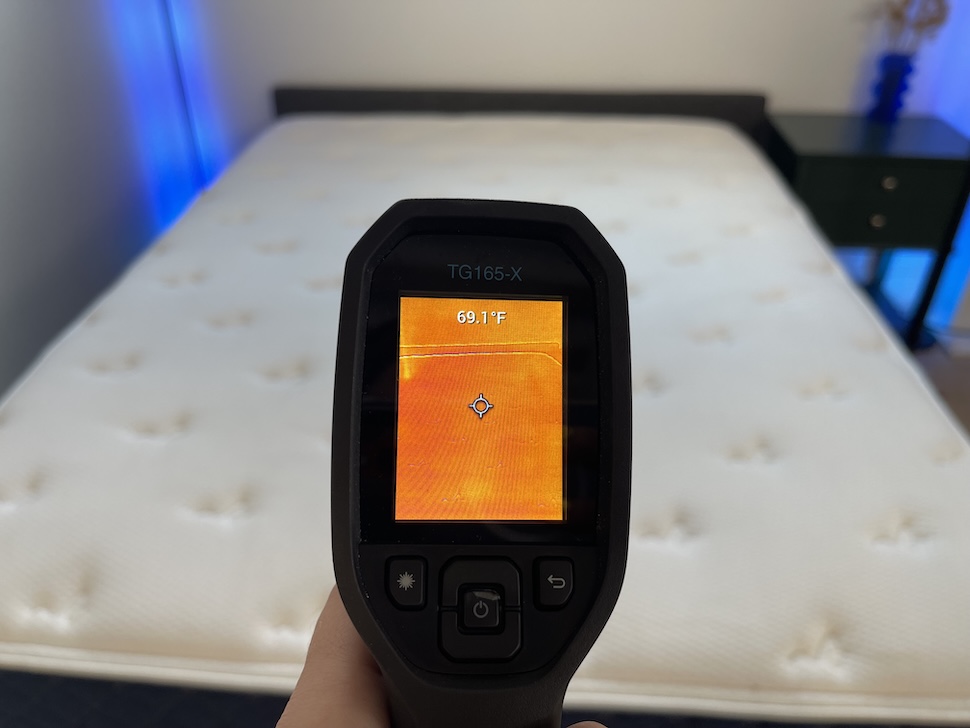 A closeup image of a hand using a thermal gun to measure the temperature of the Brooklyn Bedding Signature Hybrid. The screen reads 69.1 degrees.
