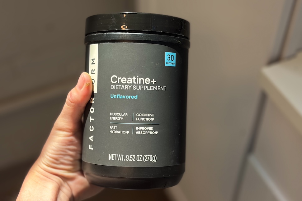 A hand holding up a black canister of Factor Form Creatine + Electrolytes