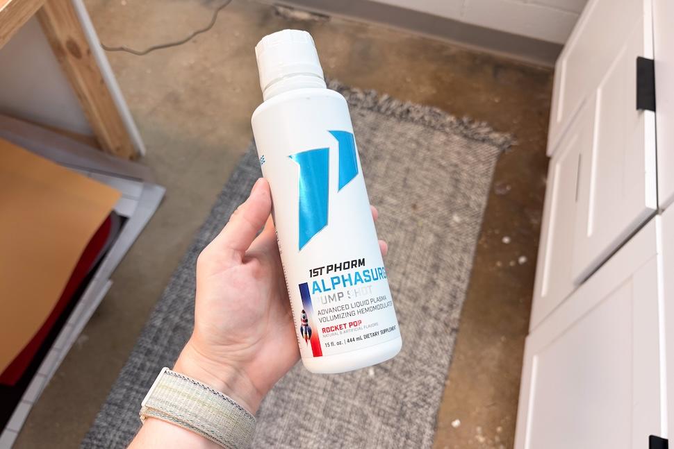 A hand holding a bottle of 1st Phorm AlphaSurge