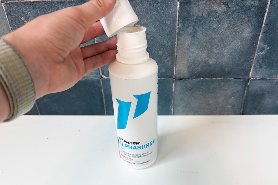 A hand lifting the cap off of a bottle of 1st Phorm AlphaSurge