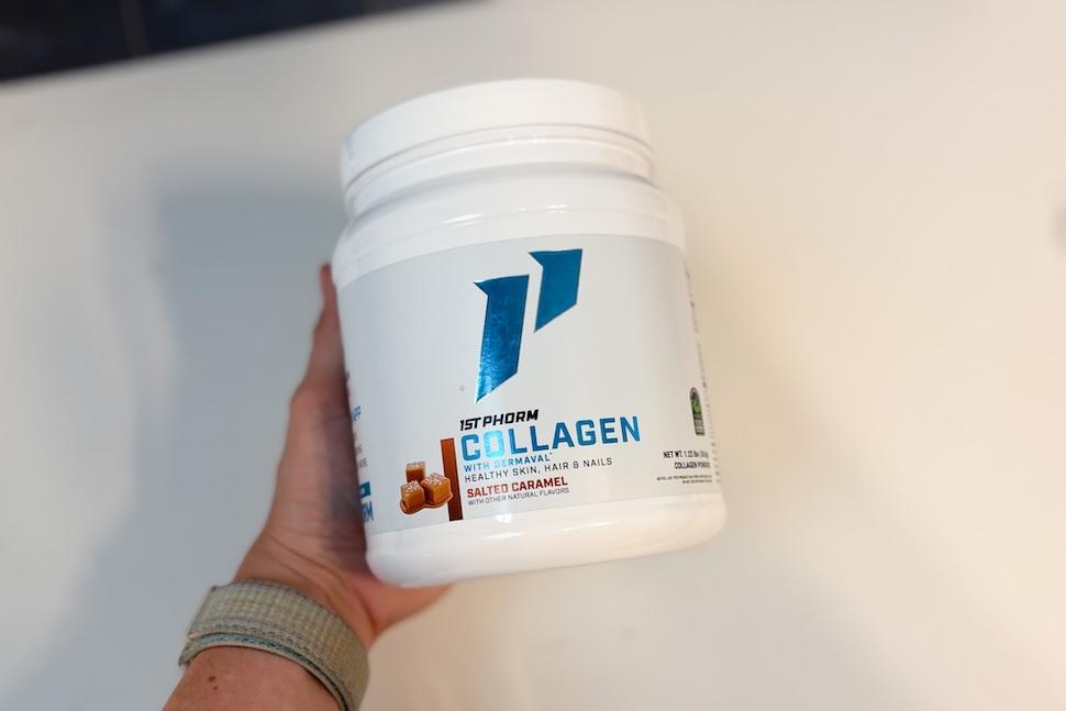 A hand holding a canister of 1st Phorm Collagen. The flavor is Salted Caramel.
