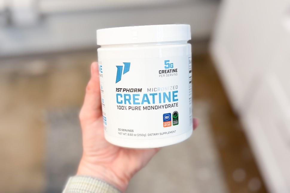 A hand holding up a canister of 1st Phorm Micronized Creatine