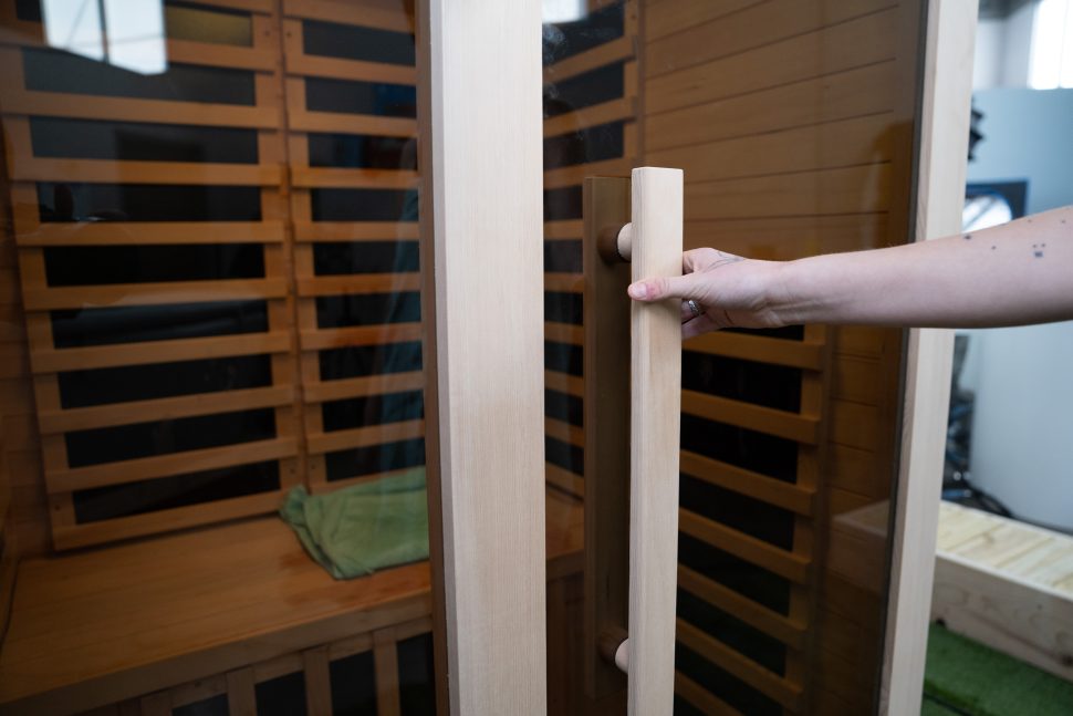 A woman about to open the glass door of the Heavenly Heat sauna