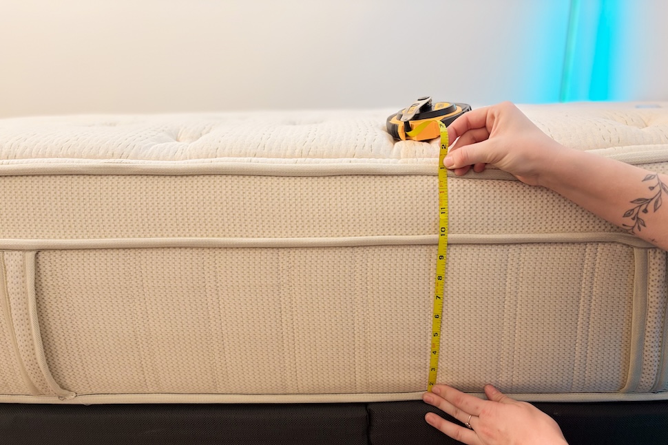 A closeup image of a woman's hands using a tape measure to measure the height of the Leesa Natural Hybrid mattress