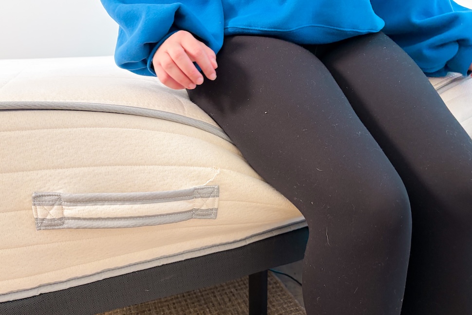 A woman sitting on the edge of the Nolah Natural mattress. The layers are sinking a bit.
