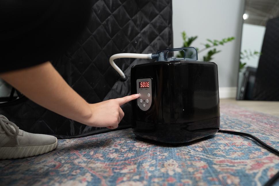 The exterior of the Sauna Box. A woman is pressing the power source to turn it on.