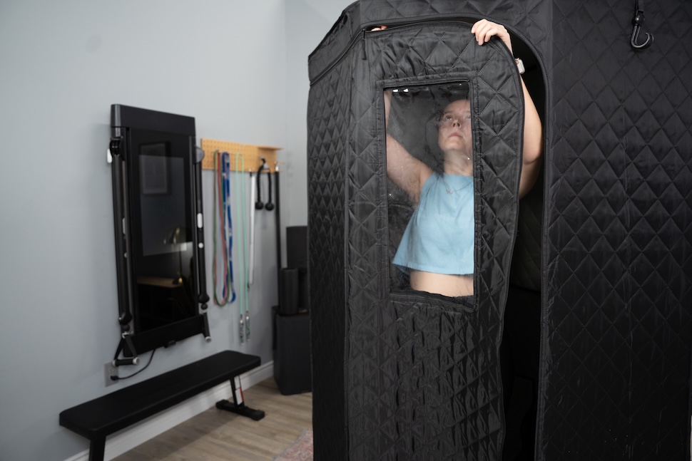 A woman standing inside the Sauna Box and zipping the door closed