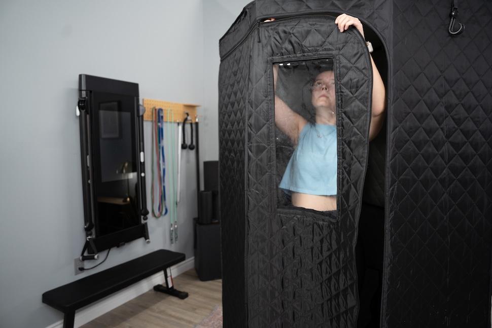 A woman standing inside the Sauna Box and zipping the door closed