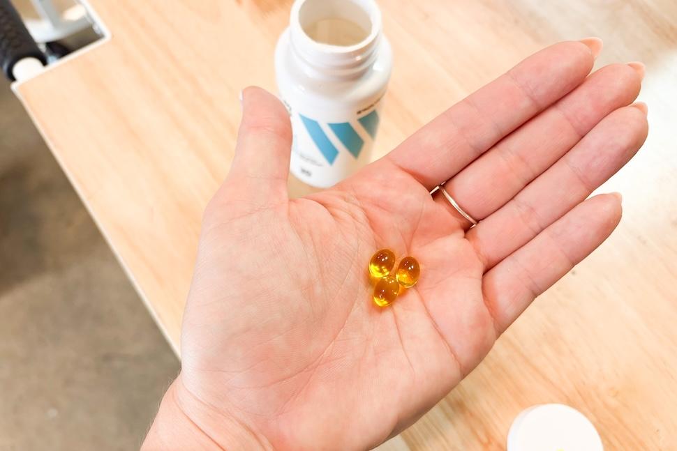 A hand holding three Swolverine Vitamin D3 capsules in its palm. The capsules are amber and transparent.
