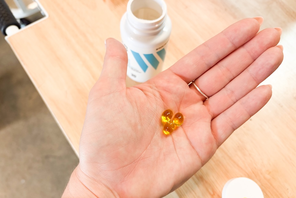 A hand holding three Swolverine Vitamin D3 capsules in its palm. The capsules are amber and transparent.