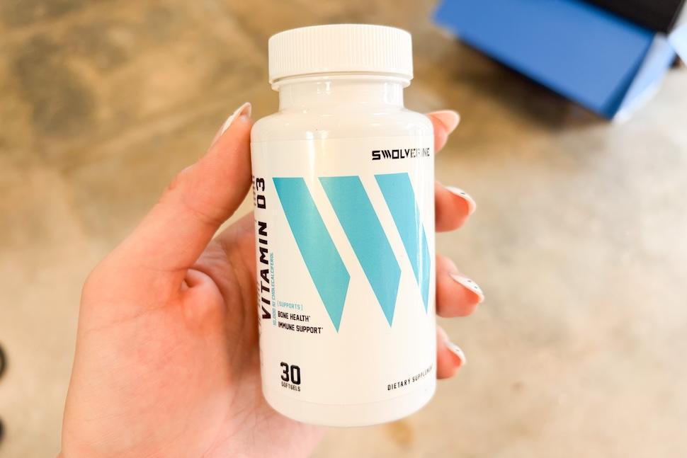 A hand holding a bottle of Swolverine Vitamin D3 capsules