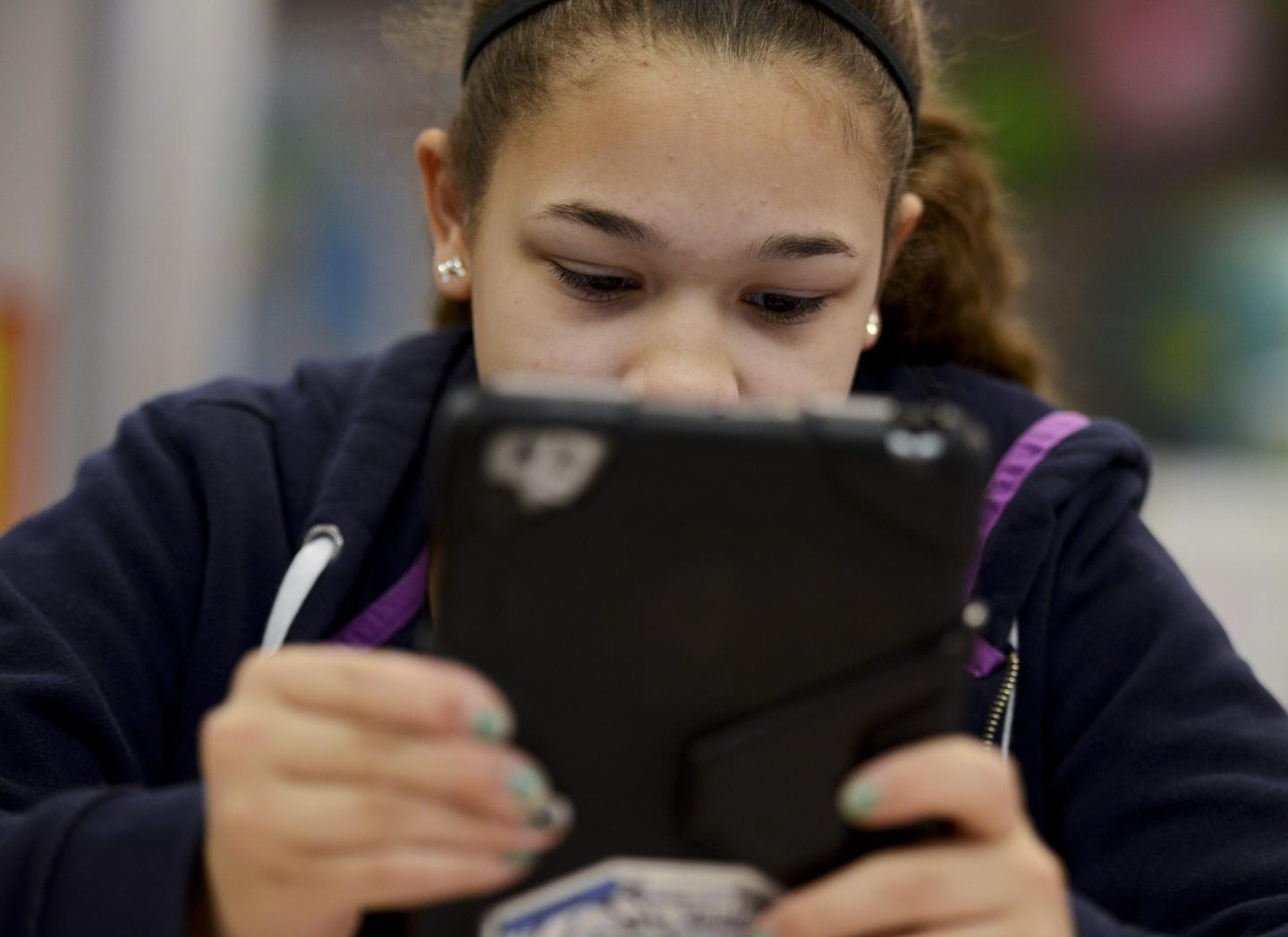 A girl holds an tablet in front of her face.