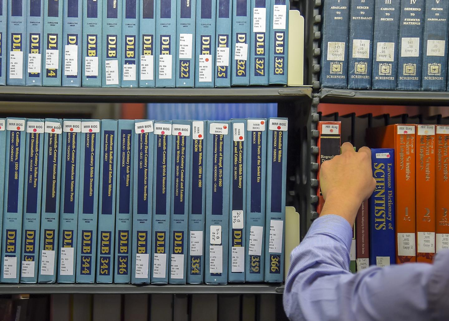 Someone leafs through titles stacked in a library