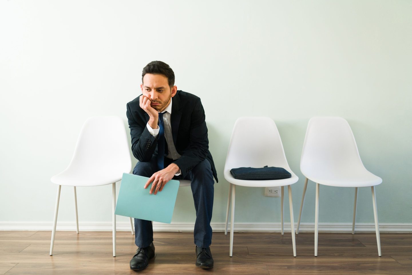 Tired hispanic man in a professional suit feeling sad while waiting for the appointment of a job interview at a recruitment office
