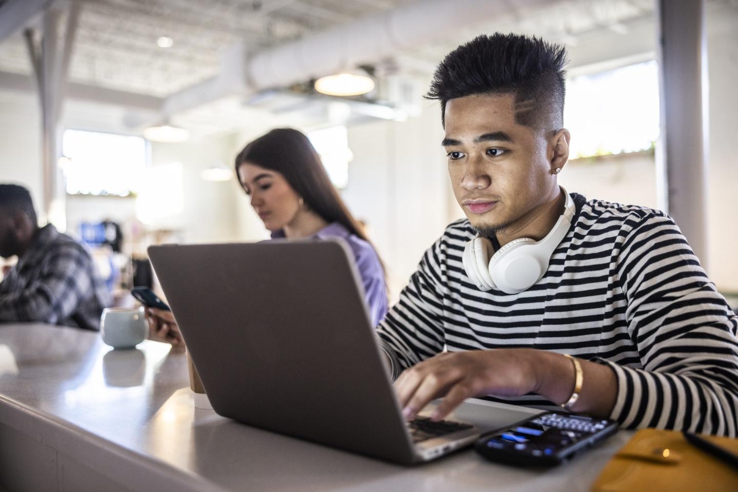 Young man working on laptop with headphones in modern coffeeshop