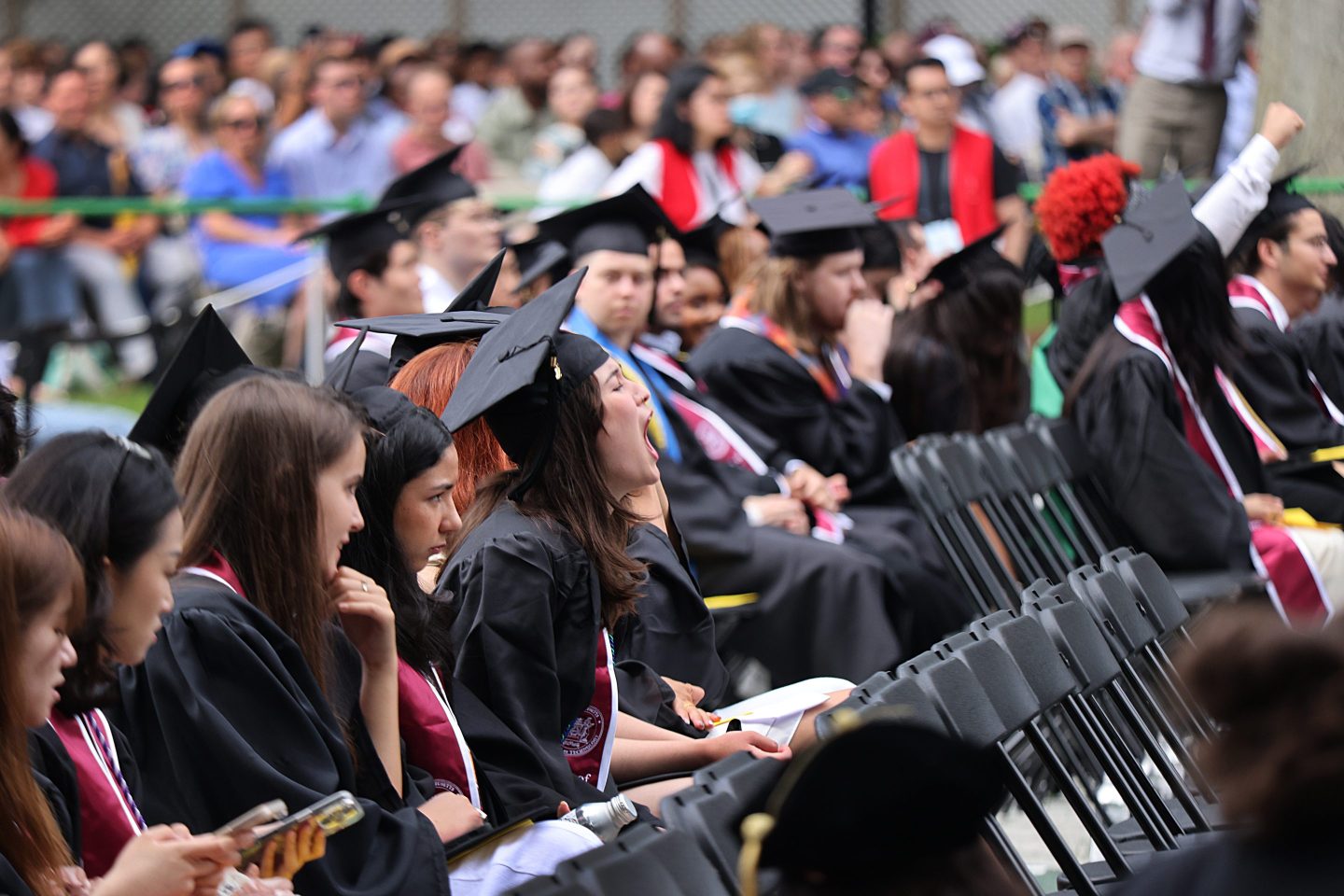 College graduates sitting at commencement yell.