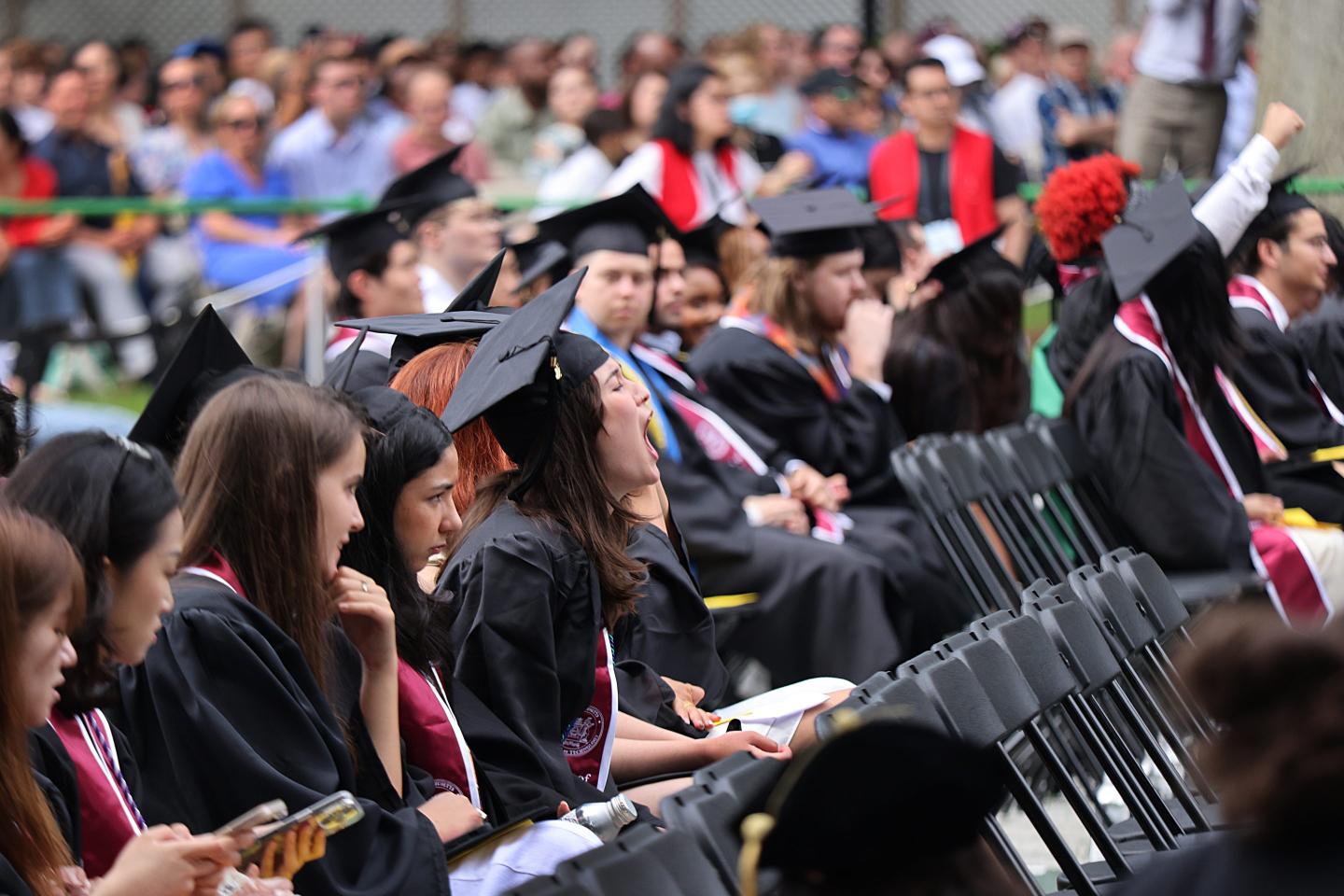 College graduates sitting at commencement yell.