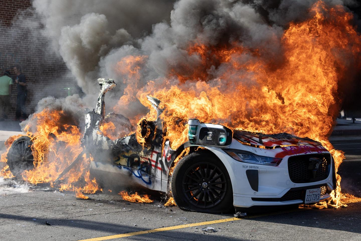 A Waymo vehicle burns as protesters clash with law enforcement in the streets surrounding the federal building during a protest in Los Angeles on June 8, 2025.