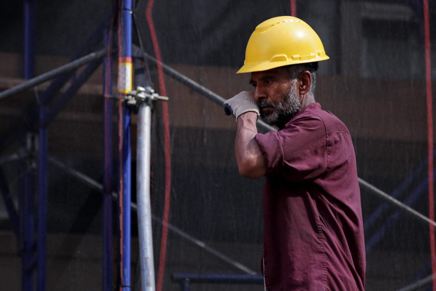 A construction worker wearing a yellow helmet wipes his nose with his hand.
