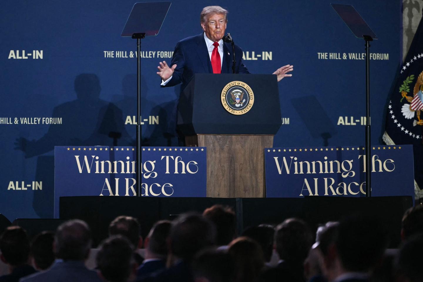 U.S. President Donald Trump speaking at a podium flanked by signs that say "Winning the AI Race."