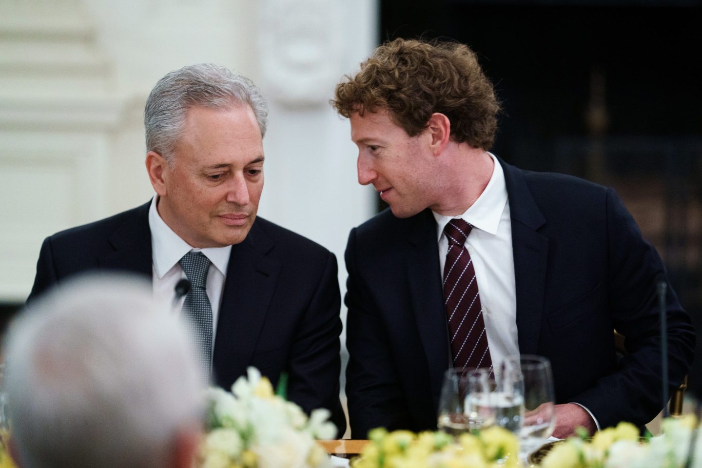 Trump AI and crpto czar David Sacks sits next to Meta CEO Mark Zuckerberg at a dinner table in the White House as Zuckerberg turns to Sacks and says something.