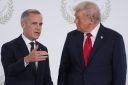 Mark Carney gestures with his hand as he stands next to Donald Trump in front of a white background.