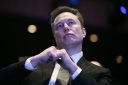 Elon Musk sits with his fists together, looking up.