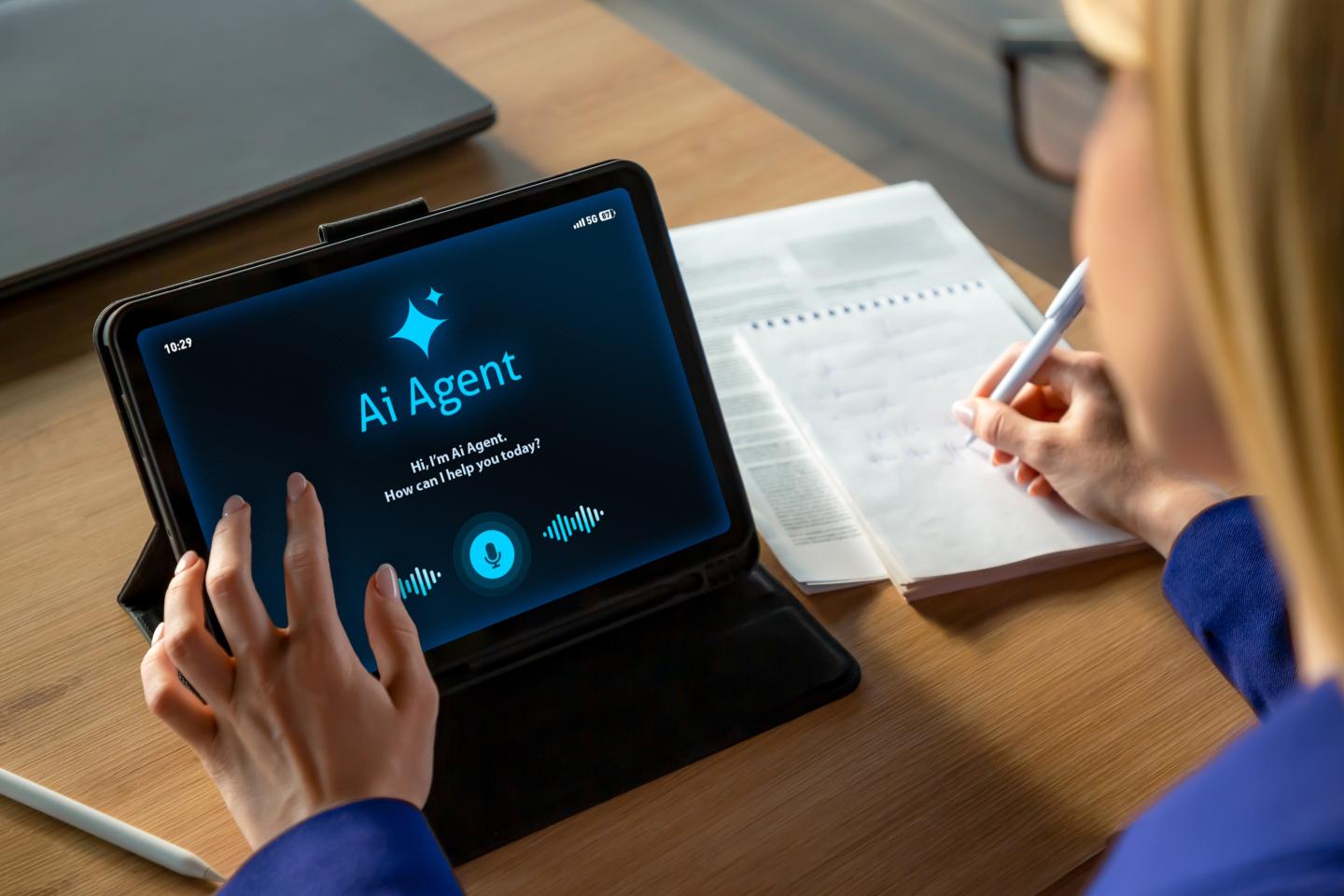 Professional businesswoman working at a desk while interacting with an AI assistant on a tablet screen. The scene shows a modern office environment with notebook, laptop, and digital tools, representing productivity, smart technology, and digital transformation in business. Ideal for concepts related to artificial intelligence, remote work, automation, business innovation, and modern office lifestyle.