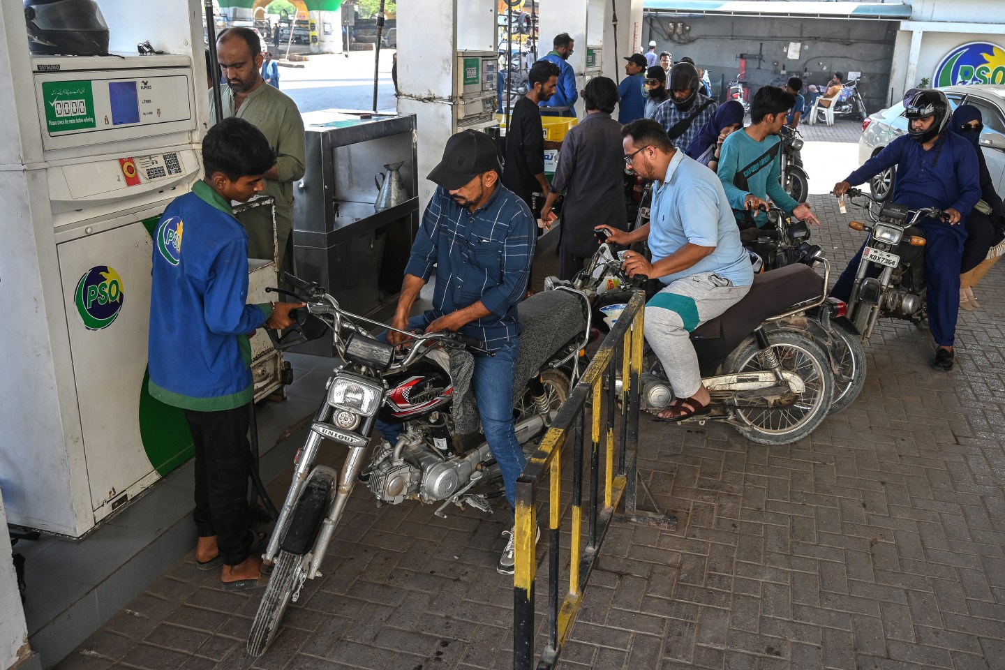 A group of people wait by a gap pump with their motorcycles.