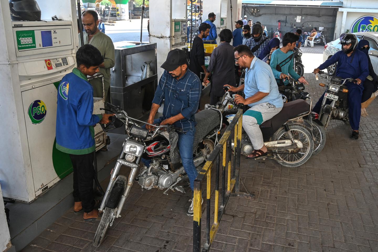 A group of people wait by a gap pump with their motorcycles.