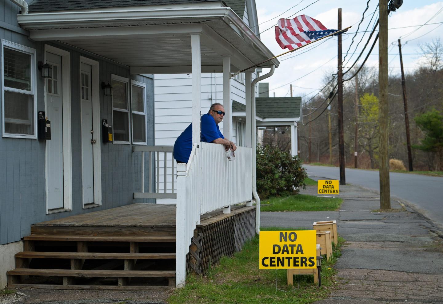 A man stands looking out over his front porch where a sign reads, "No data centers."