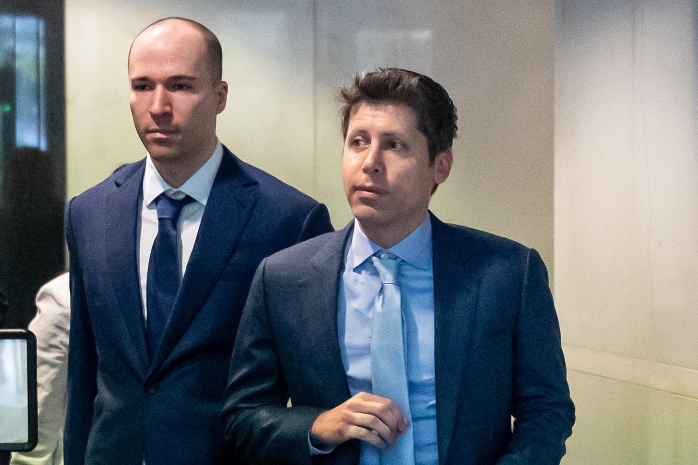 OpenAI cofounder and president Greg Brockman (left) and cofounder and CEO Sam Altman (right) dressed in suits and walking through the lobby of a court house.