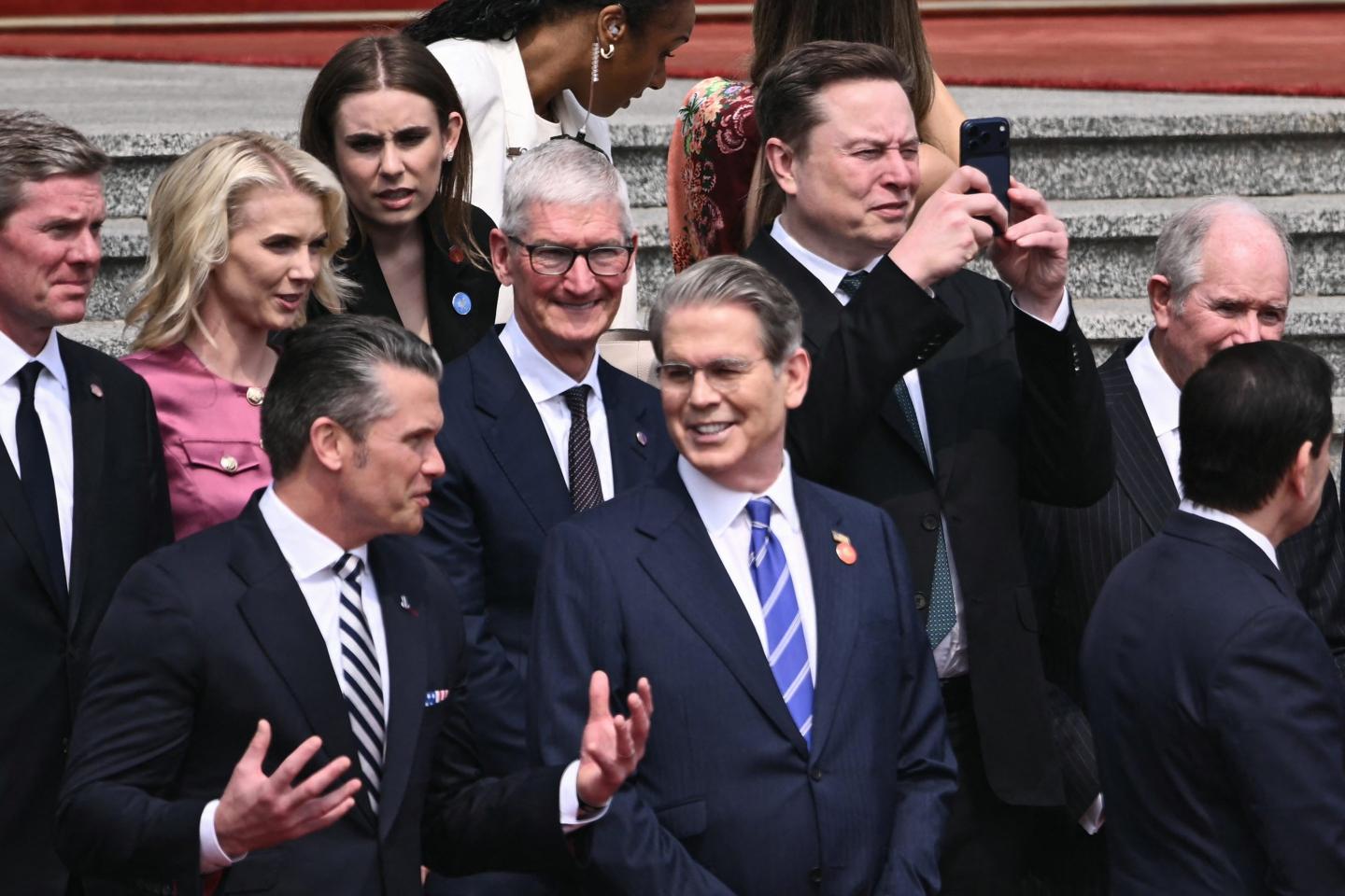 US Secretary of Defense Pete Hegseth (bottom L) speaks with US Treasury Secretary Scott Bessent (bottom centre R), as Tesla and SpaceX CEO Elon Musk (top R) uses his phone and Apple CEO Tim Cook (C) looks on at a welcome ceremony for US President Donald Trump at the Great Hall of the People in Beijing on May 14, 2026.