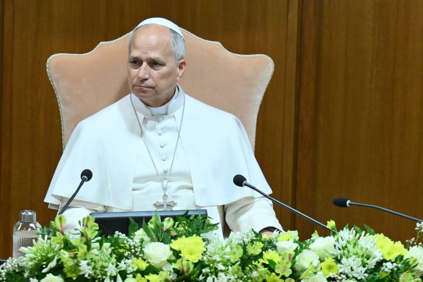 Pope Leo XIV presenting his 'AI encyclical' at the Vatican in Rome. The Pope, dressed in white, is sitting in a large chair with a laptop open in front of him and flowers arranged on the table in front of the laptop,