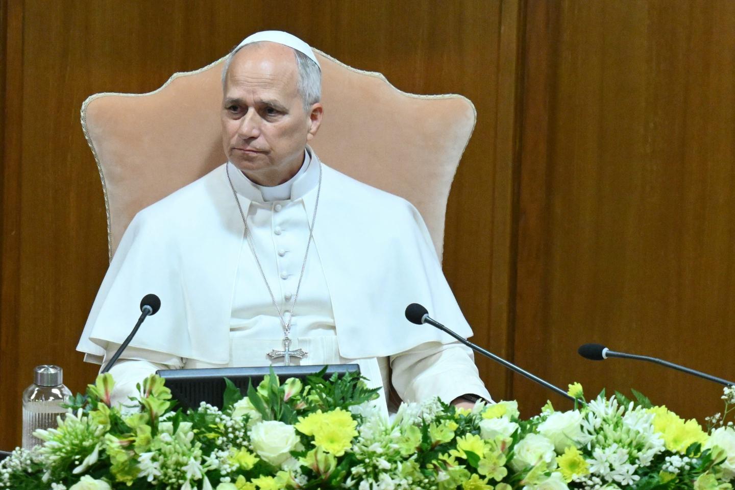 Pope Leo XIV presenting his 'AI encyclical' at the Vatican in Rome. The Pope, dressed in white, is sitting in a large chair with a laptop open in front of him and flowers arranged on the table in front of the laptop,