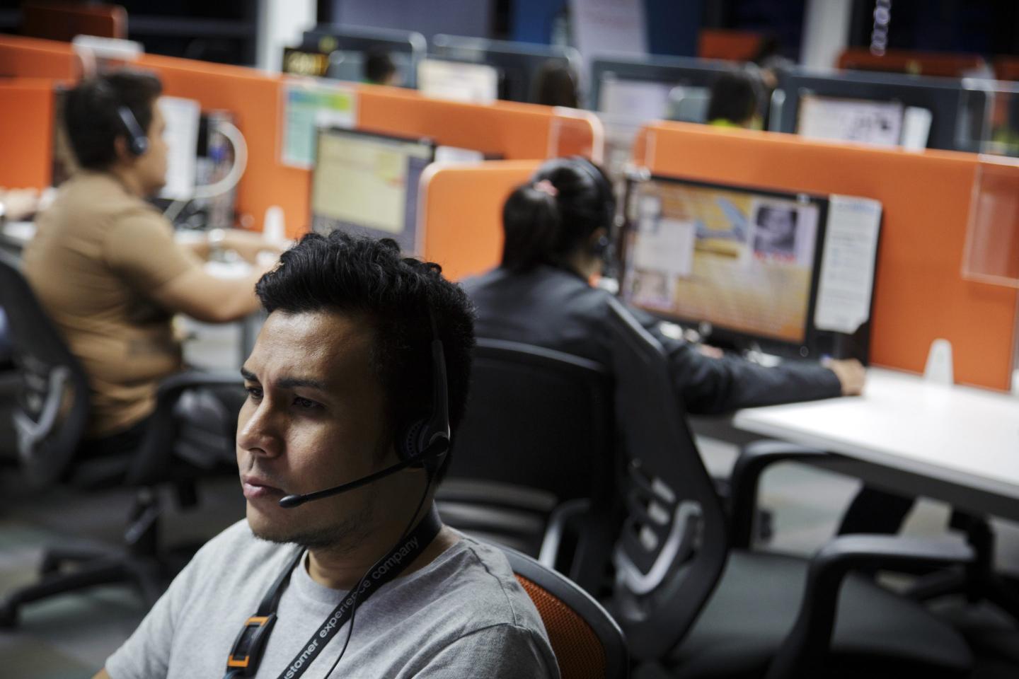 A man with a headset sits at a desk in a call center.