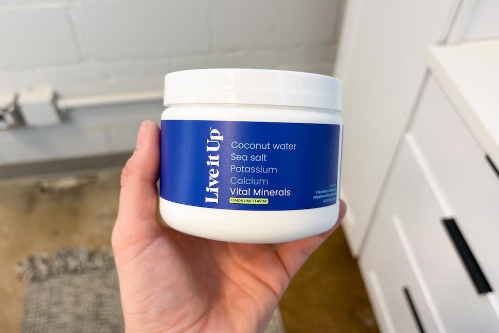A hand holding up a canister of Live it Up Vital Minerals