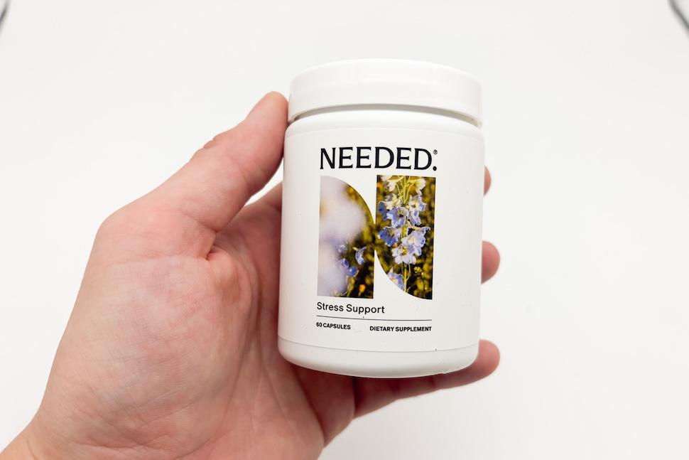 A hand holding a canister of Needed Stress Support supplements