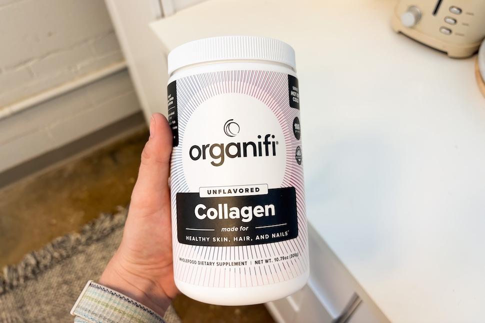 A hand holding a canister of Organifi Unflavored Collagen