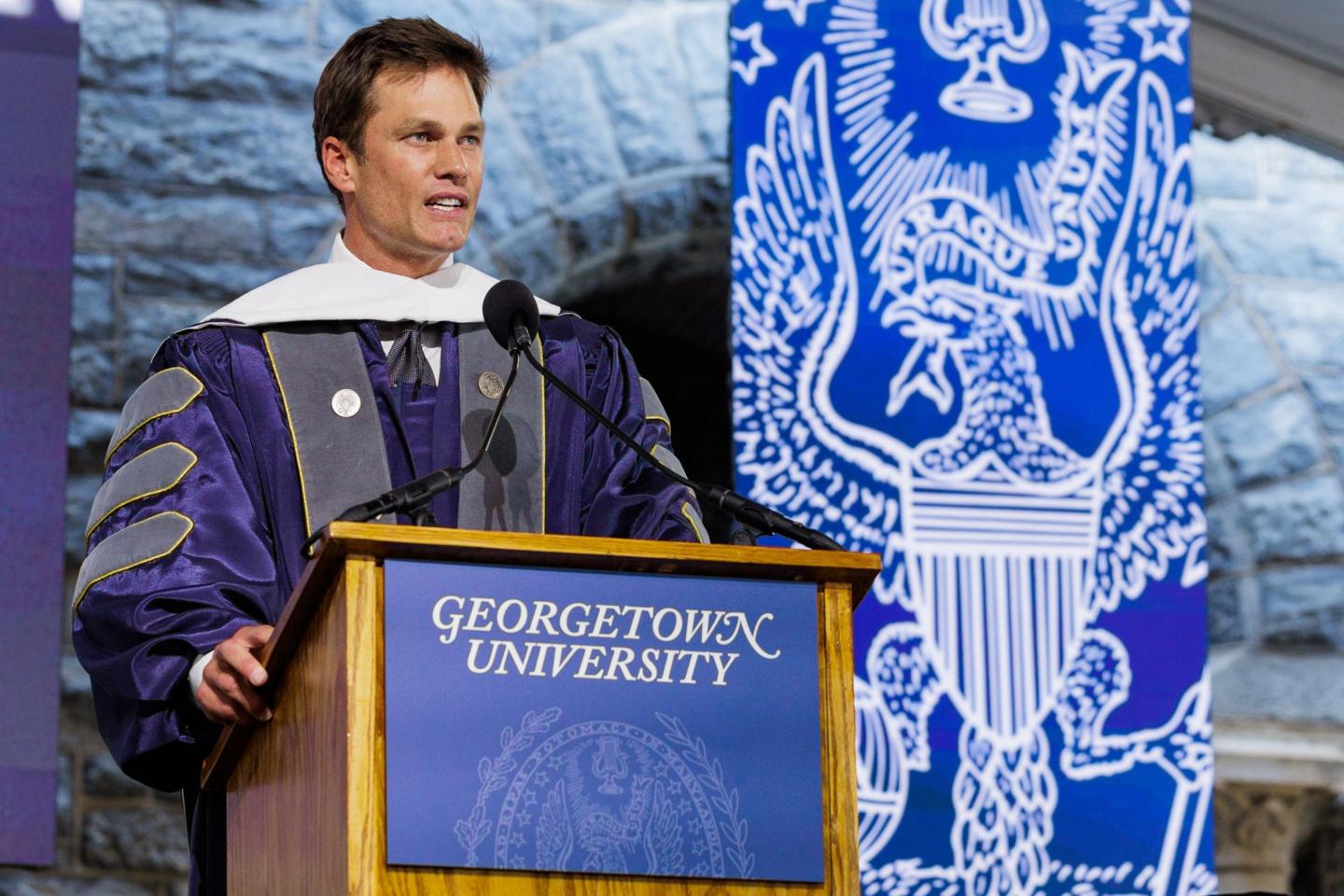 Tom Brady wearing commencement regalia behind a podium at Georgetown University
