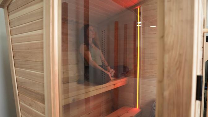 A woman sitting behind the closed glass door of the Plunge Sauna