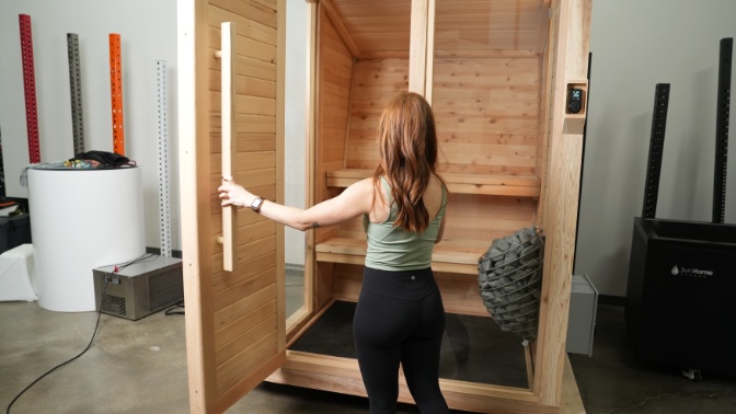 A woman opening the door to the wooden Plunge Sauna
