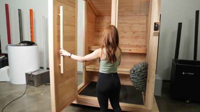 A woman opening the door to the wooden Plunge Sauna