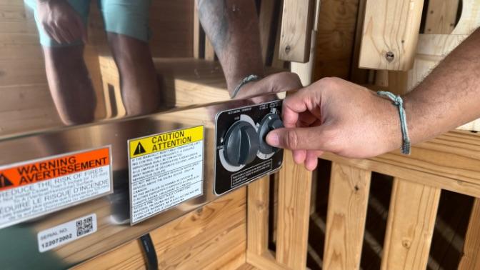 A closeup of a hand turning the temperature dial on the Redwood Outdoor Sauna