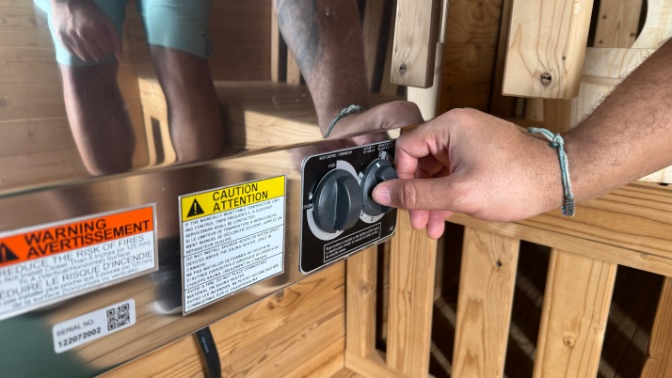 A closeup of a hand turning the temperature dial on the Redwood Outdoor Sauna