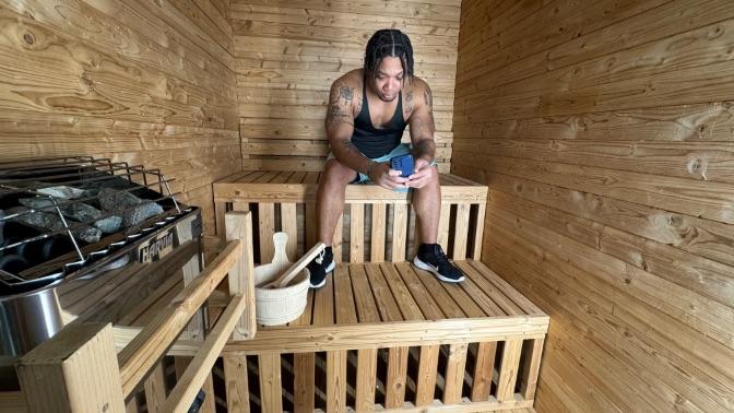 A man sitting in the Redwood Outdoor sauna, looking at his phone