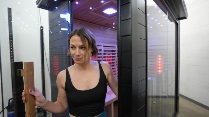 A woman walking out of the glass door of the Sun Home Luna 5-Person Outdoor Sauna.