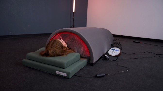 A woman lying inside the Sunlighten Solo Sauna. You can see the sauna glowing from inside.