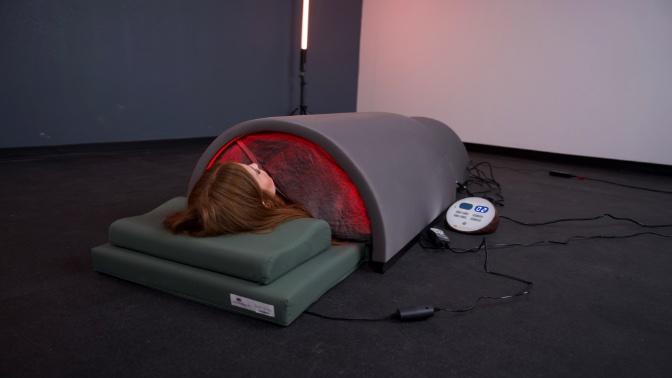 A woman lying inside the Sunlighten Solo Sauna. You can see the sauna glowing from inside.